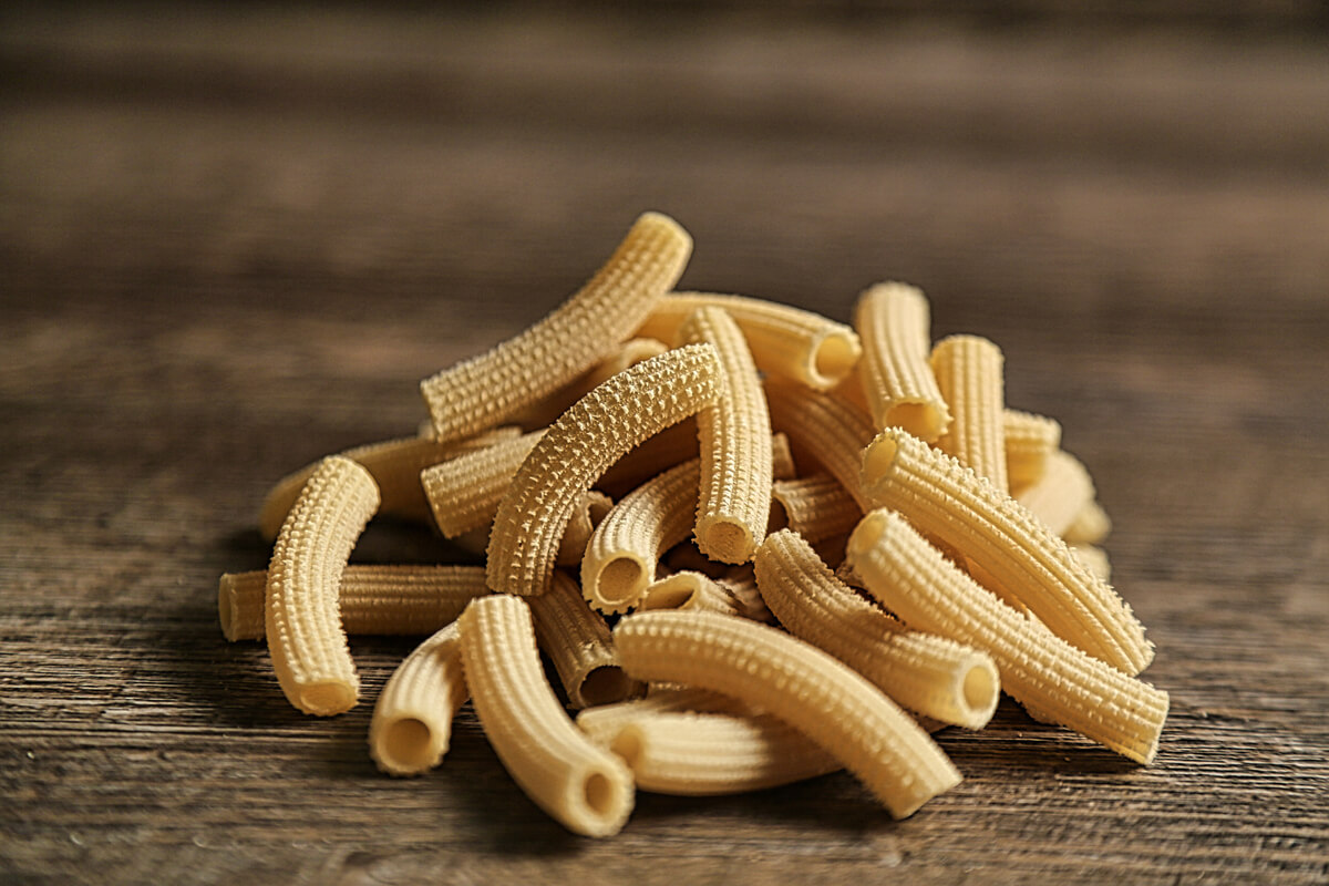 Rigatoni pasta is tubular in shape and loved for its ability to hold sauces and grated cheese on its ridges. It resembles penne but with square-cut ends and often slightly curved. Rigatoni is the favorite pasta shape in the south of Italy and Sicily. It is perfect with any sauce, from cream to the chunkiest meat sauces.